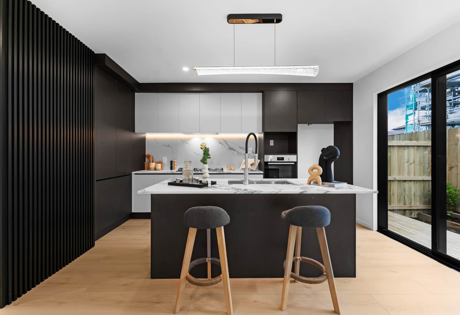 Black kitchen with timber slat wall, marble-look island and timber stools