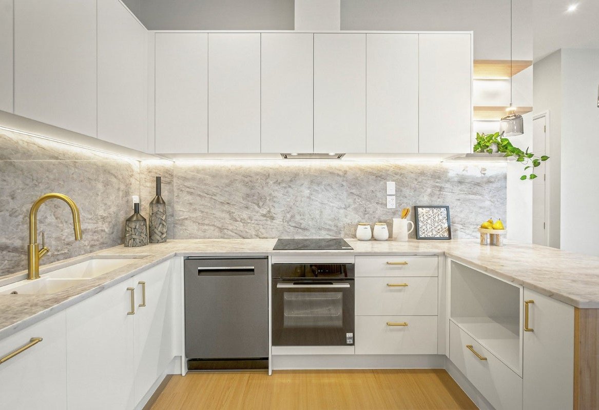 White U-shaped kitchen with brushed gold handles and stone splashback